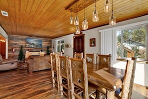 Una mesa de comedor de madera con sillas, techo de madera y un ventanal con vistas a una casa.