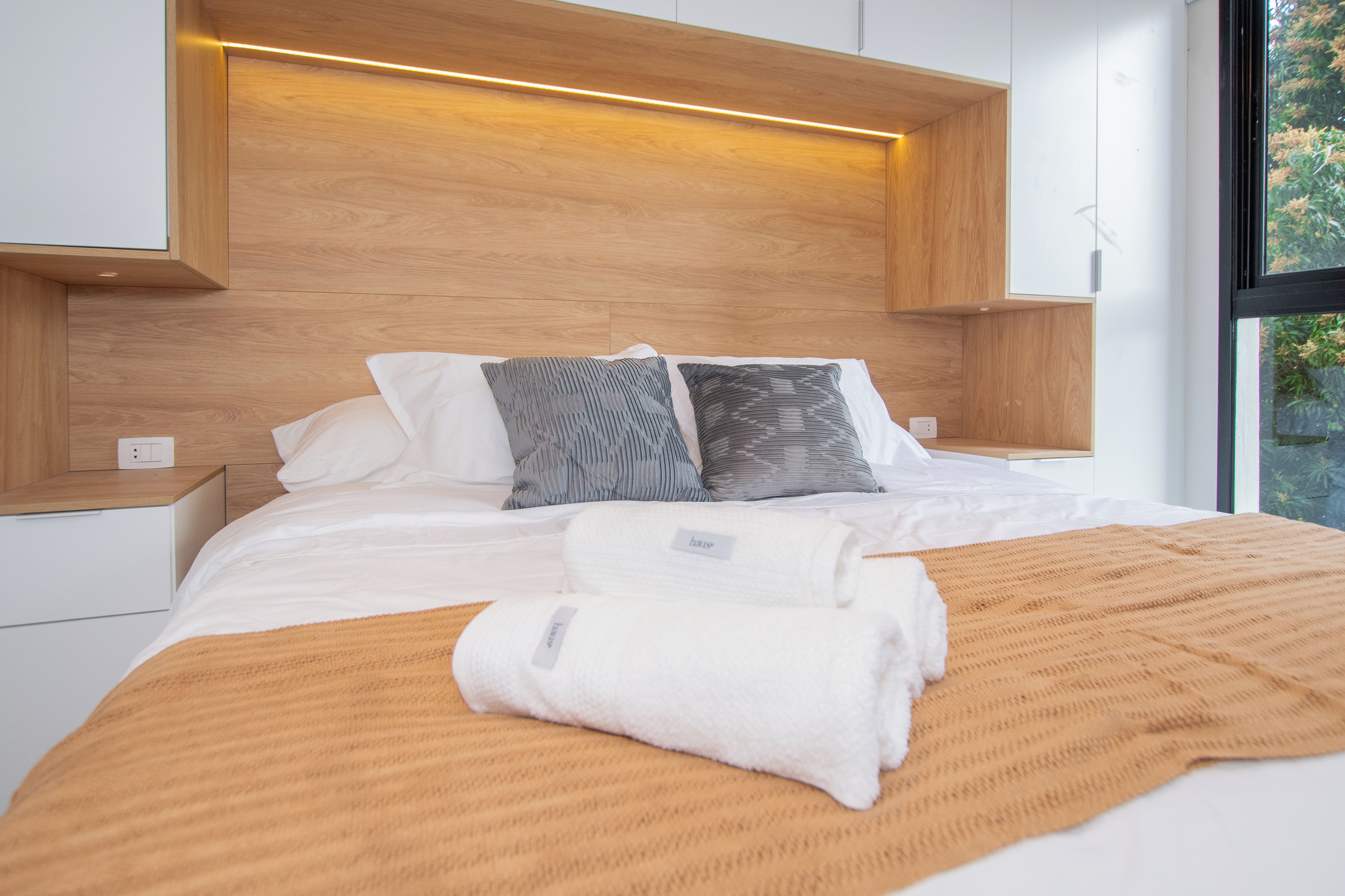 Ein modernes Schlafzimmer mit einem hölzernen Kopfteil, einem großen Bett mit weißer Bettwäsche, zwei Kissen und einem gefalteten Handtuch.