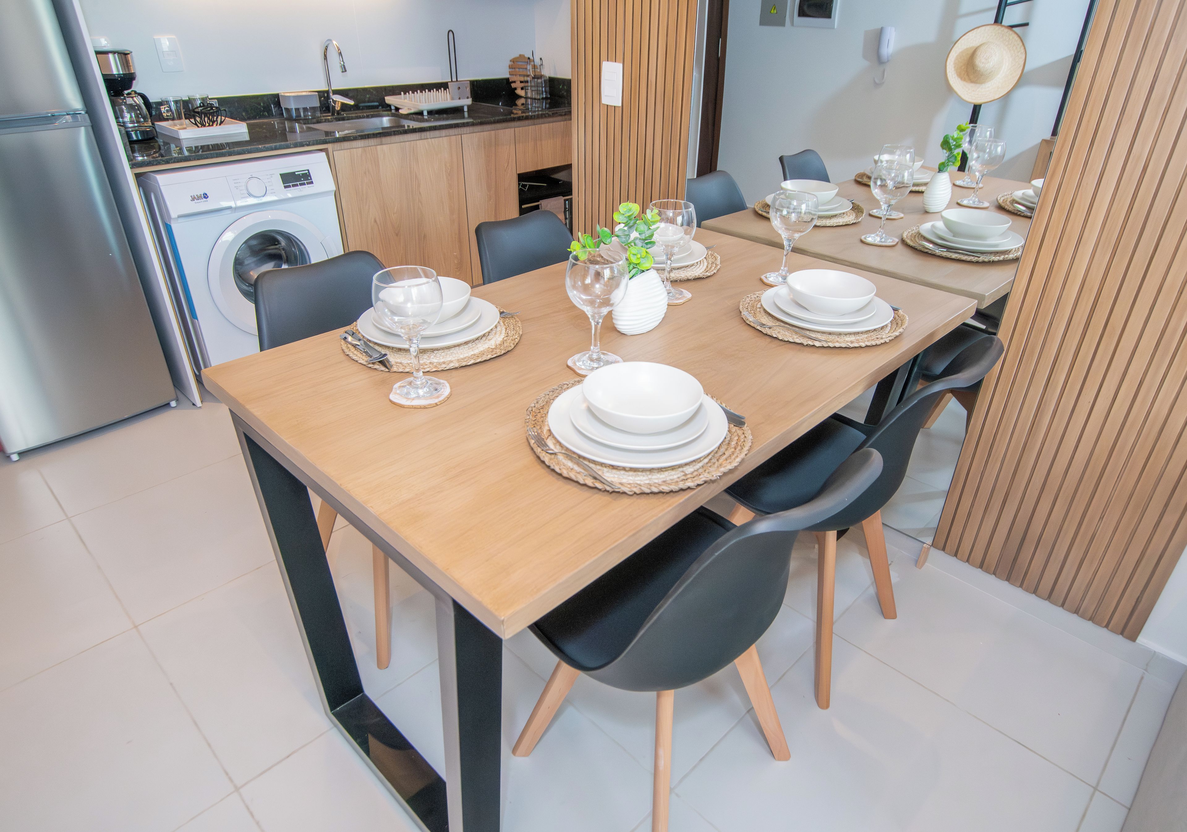 A dining area with a wooden table set for six, surrounded by black chairs.
