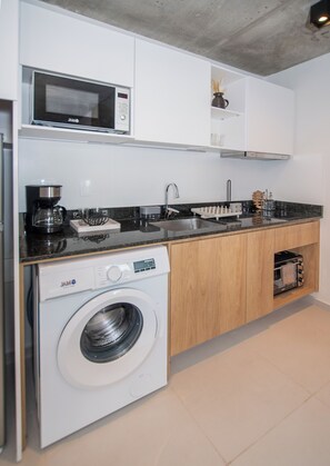 A compact kitchen with a built-in washer, a microwave, and a coffee maker. - Corporate Stays First del Sol - 107 (Asunción)