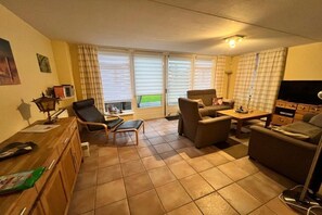 A living room with a sofa, armchairs, a coffee table, a TV, and a window with blinds. - Holiday home with 3 bedrooms (Medemblik)