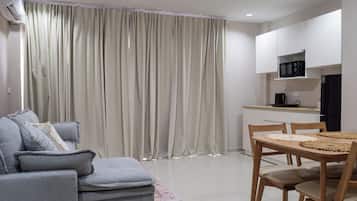 A modern living room with a grey sofa, a dining table with chairs, and a kitchen area with a microwave.