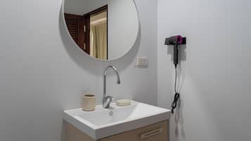 A bathroom with a white sink, a round mirror, a faucet, a cup, and a hairdryer plugged into the wall.