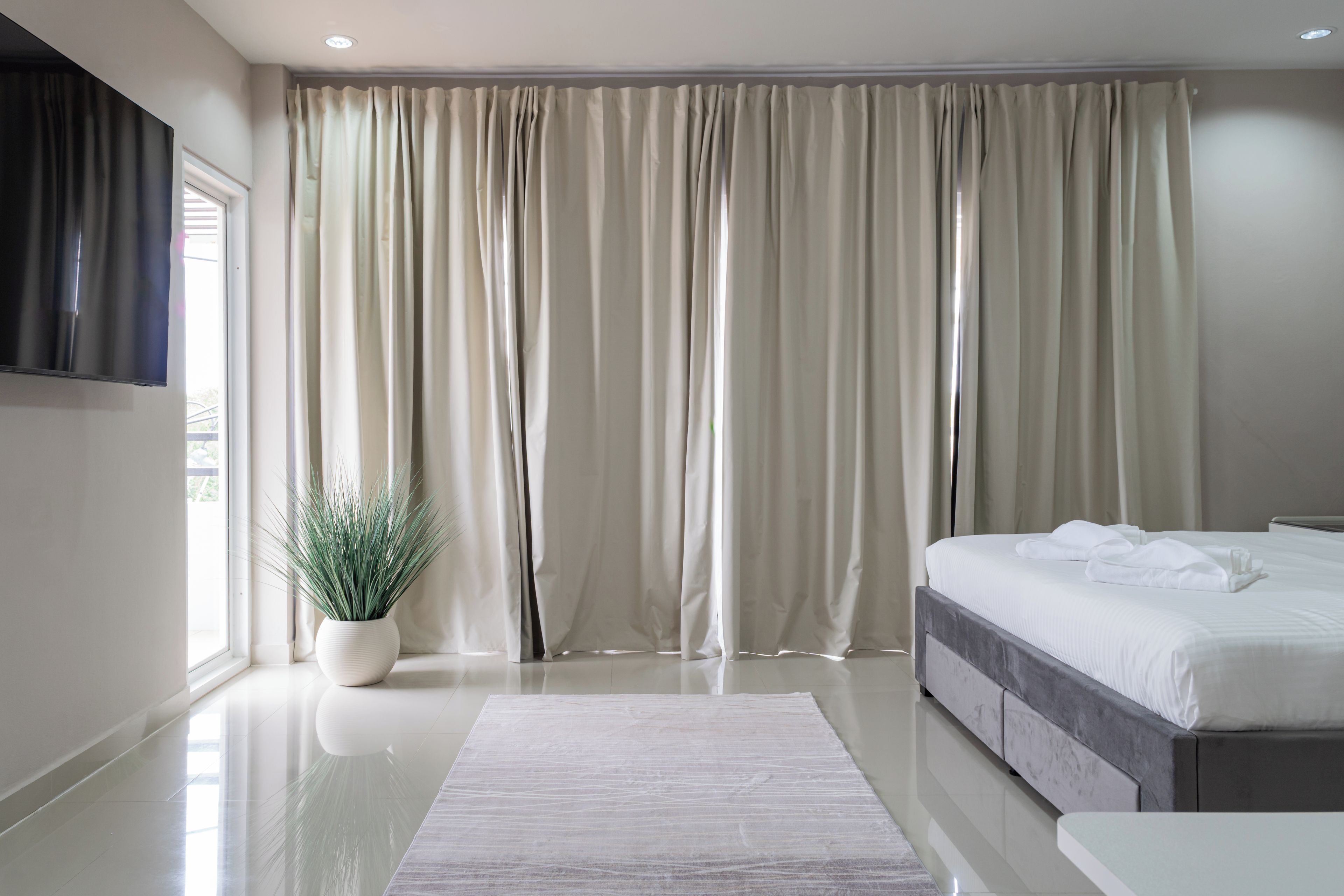 A modern bedroom with a large bed, a flat-screen TV mounted on the wall, and a potted plant.