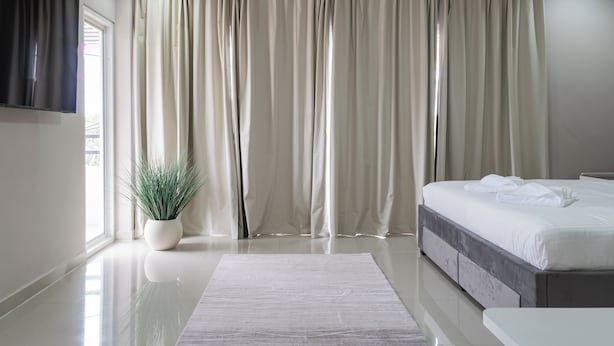A modern bedroom with a large bed, a flat-screen TV mounted on the wall, and a potted plant. - The One Sky  (Rawai)