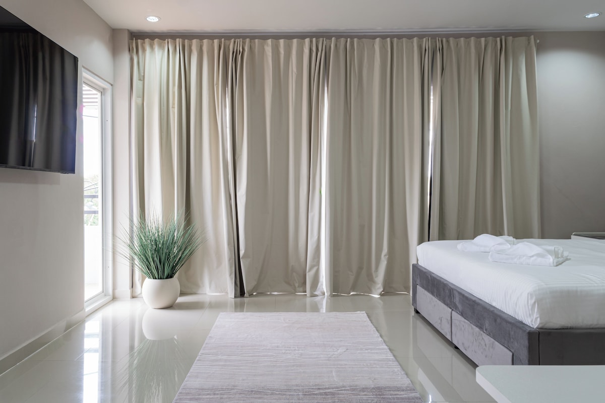 A modern bedroom with a large bed, a flat-screen TV mounted on the wall, and a potted plant.