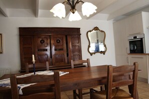 Un comedor con mesa y sillas de madera, una lámpara de araña, un espejo grande y una cocina con armarios y horno.
