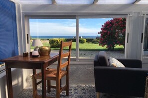Ein Zimmer mit Tisch und Stuhl, einer Couch und Blick ins Freie durch eine Glastür.