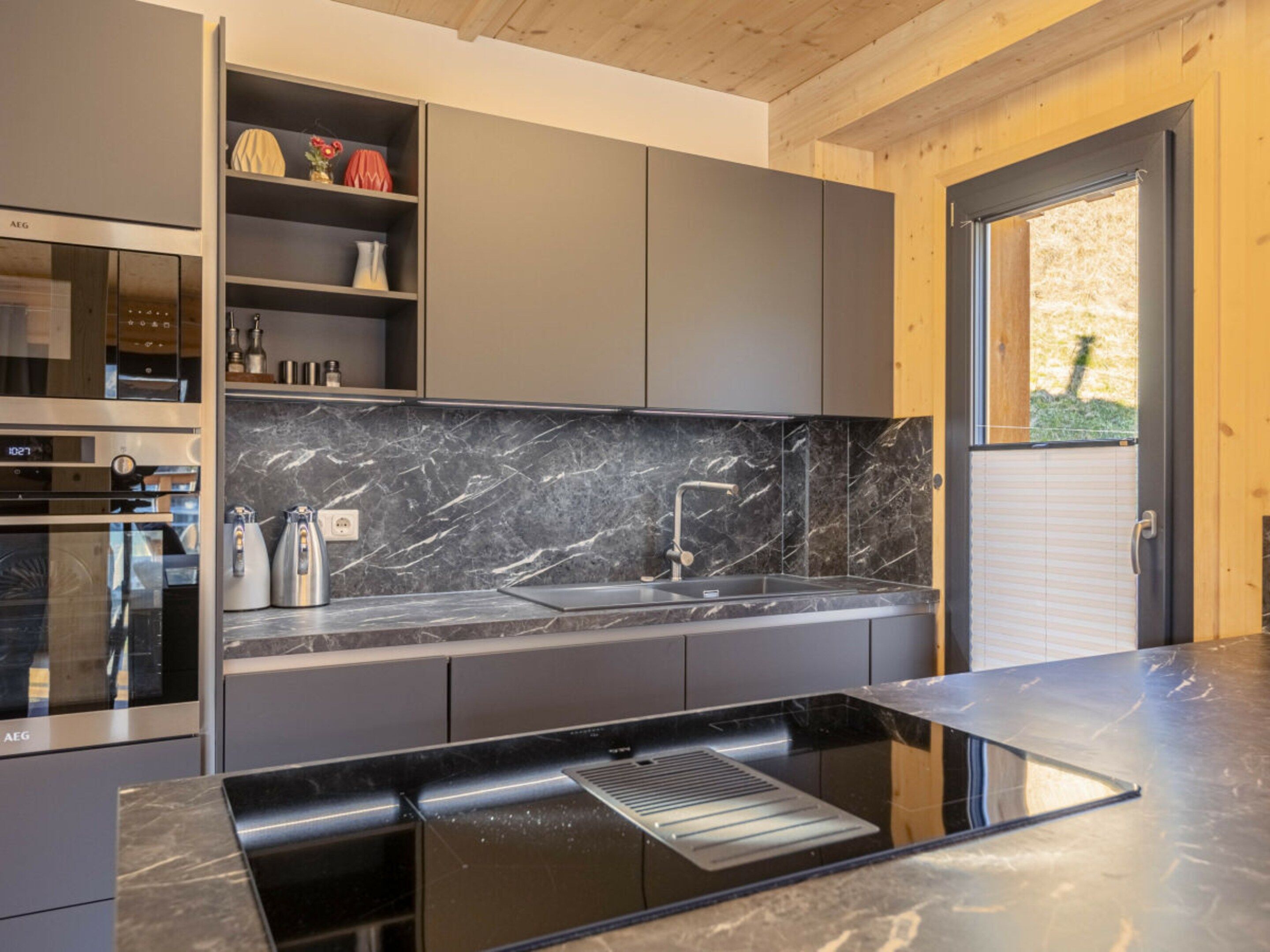Una cocina moderna con horno empotrado, pileta de acero inoxidable y salpicadero de mármol.