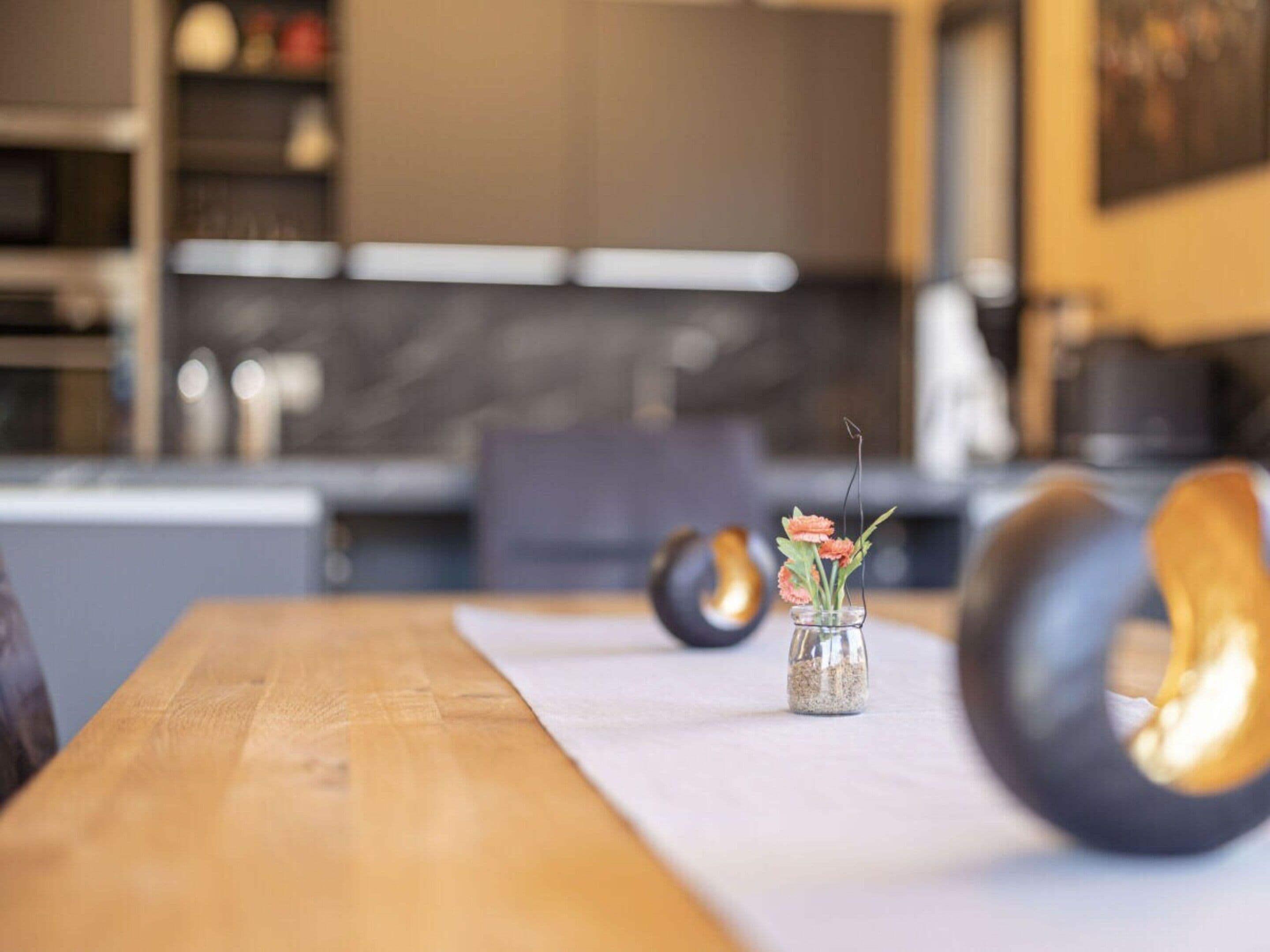 A modern kitchen with a wooden table, a vase with flowers, and a unique black chair.