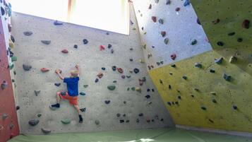Un gimnasio de escalada con suelo acolchado, paredes para escalar y un ventanal.