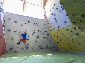 Ein Kletterzentrum mit gepolstertem Boden, Kletterwänden und einem Fenster.