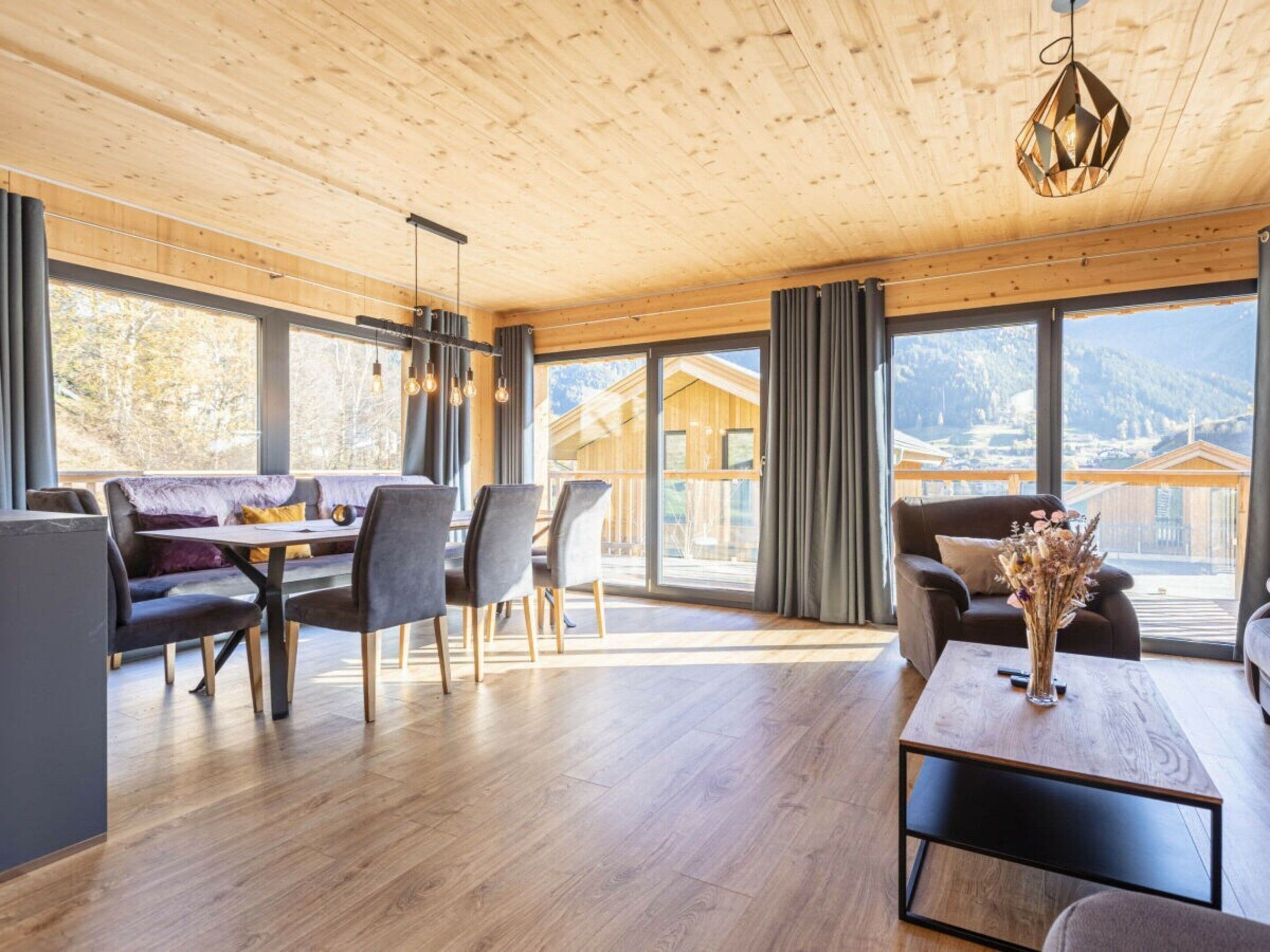 Amplia habitación con techo de madera, zona de comedor con mesa y sillas, y ventanas grandes con vistas a las montañas.