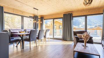 Amplia habitación con techo de madera, zona de comedor con mesa y sillas, y ventanas grandes con vistas a las montañas.