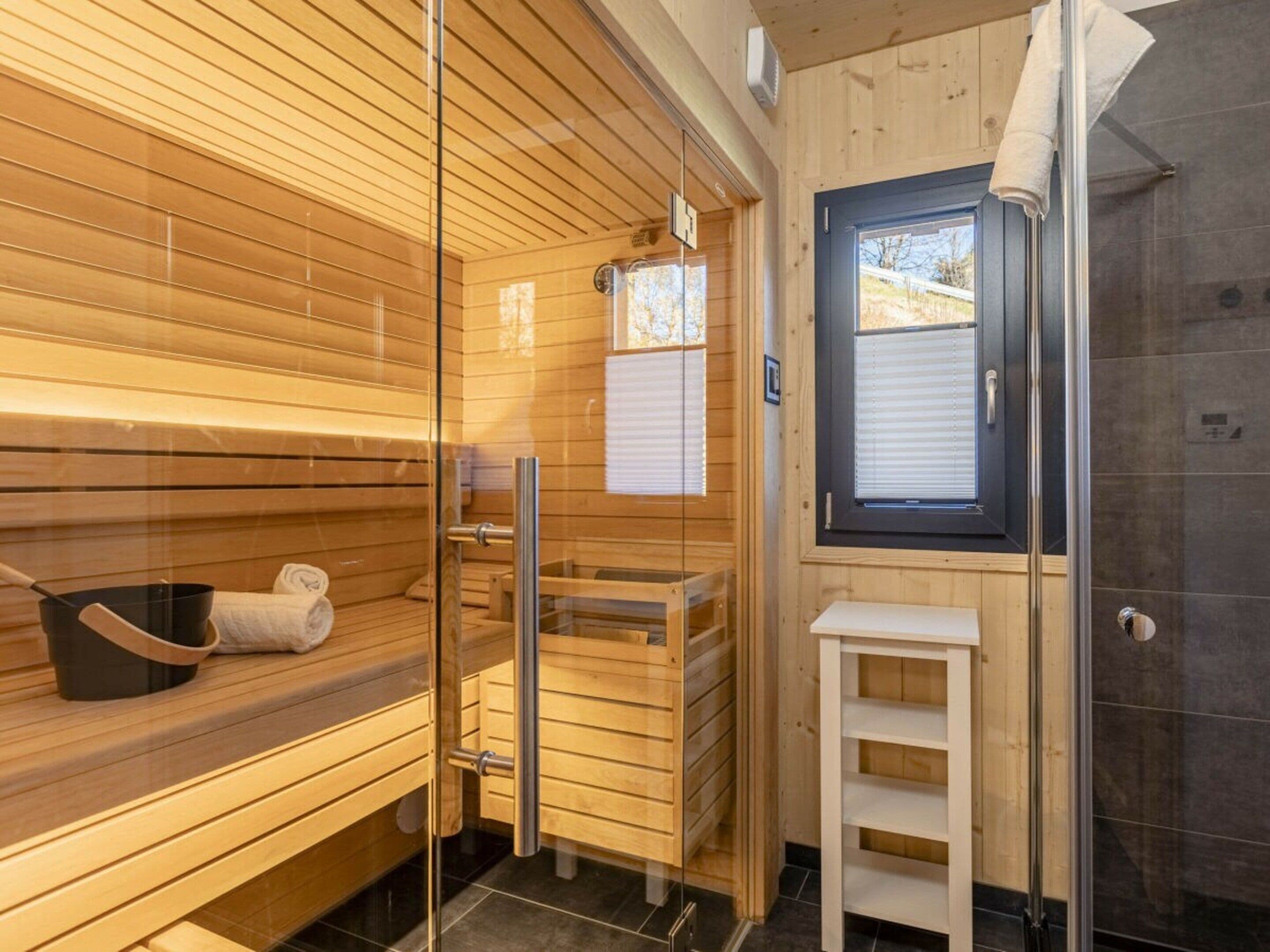 A sauna room with wooden benches, a glass door, and a small table with a towel and a pot.