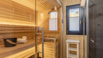 A sauna room with wooden benches, a glass door, and a small table with a towel and a pot.