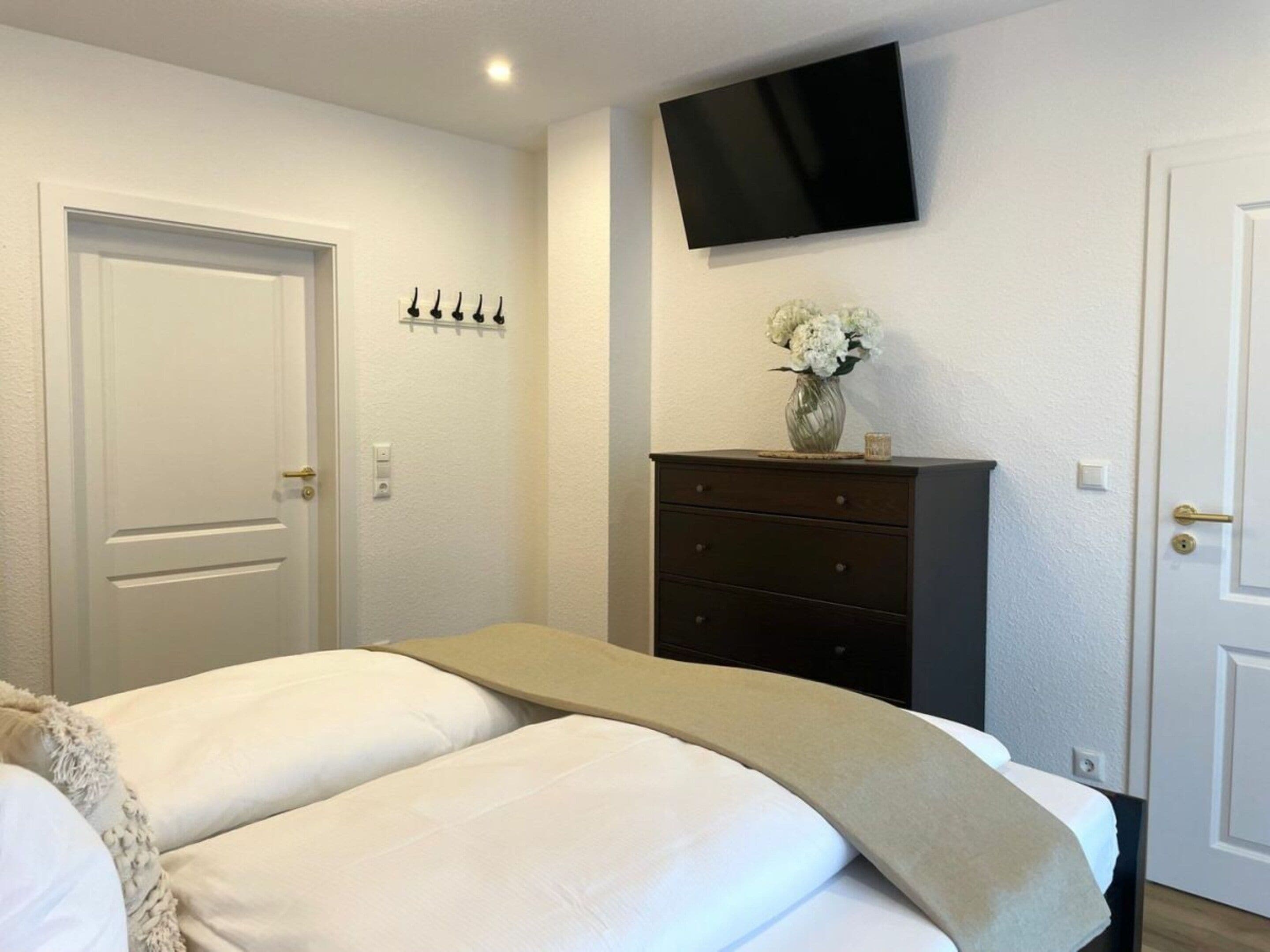 A bedroom with a bed, a dresser, a television mounted on the wall, and a door.