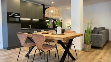 Una cocina moderna con armarios oscuros, una mesa de comedor de madera, sillas de mimbre y una lámpara colgante.