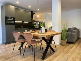A modern kitchen with dark cabinets, a wooden dining table, wicker chairs, and a hanging light fixture.