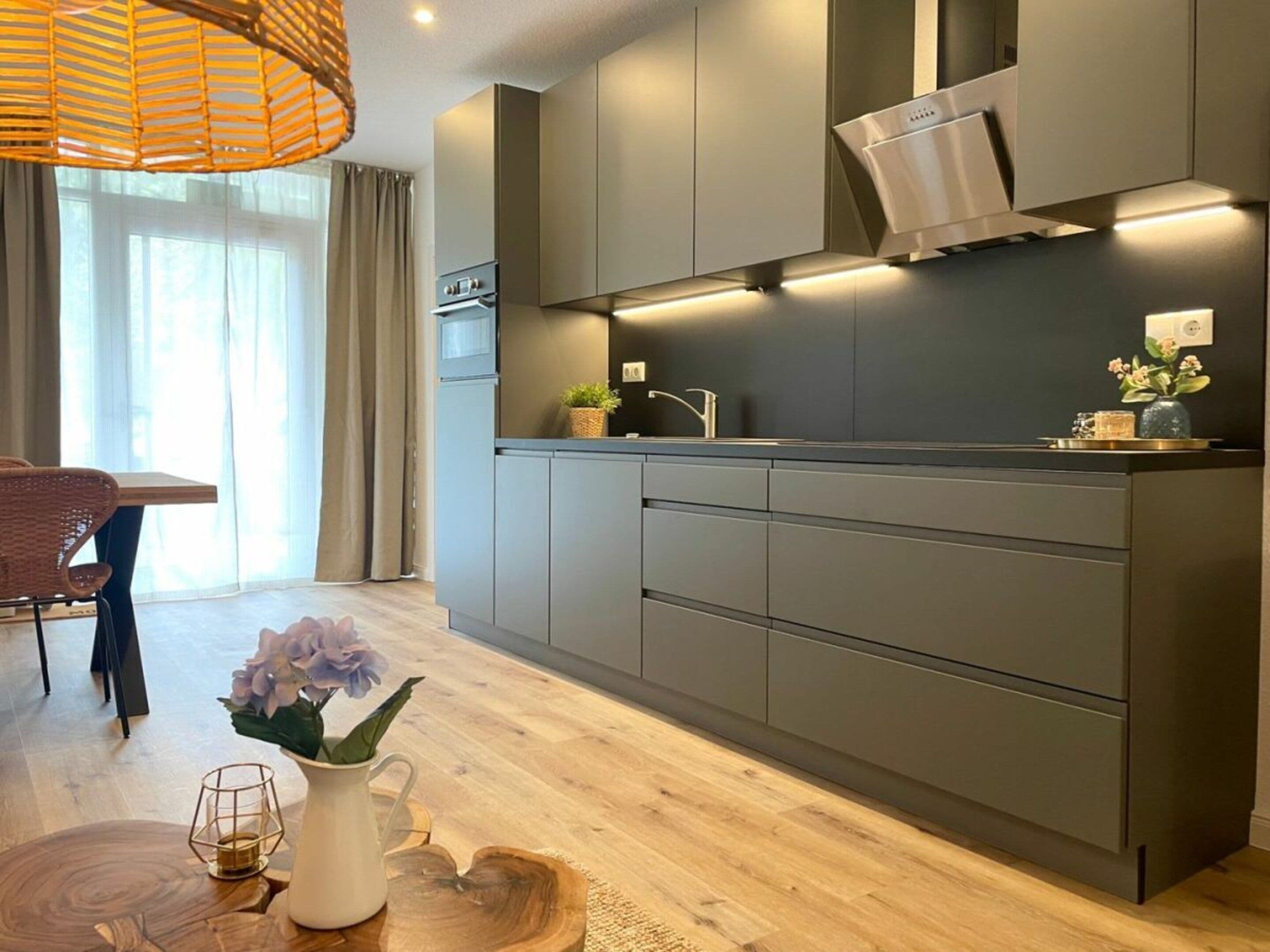 A modern kitchen with grey cabinetry, a built-in oven, and a pendant light.