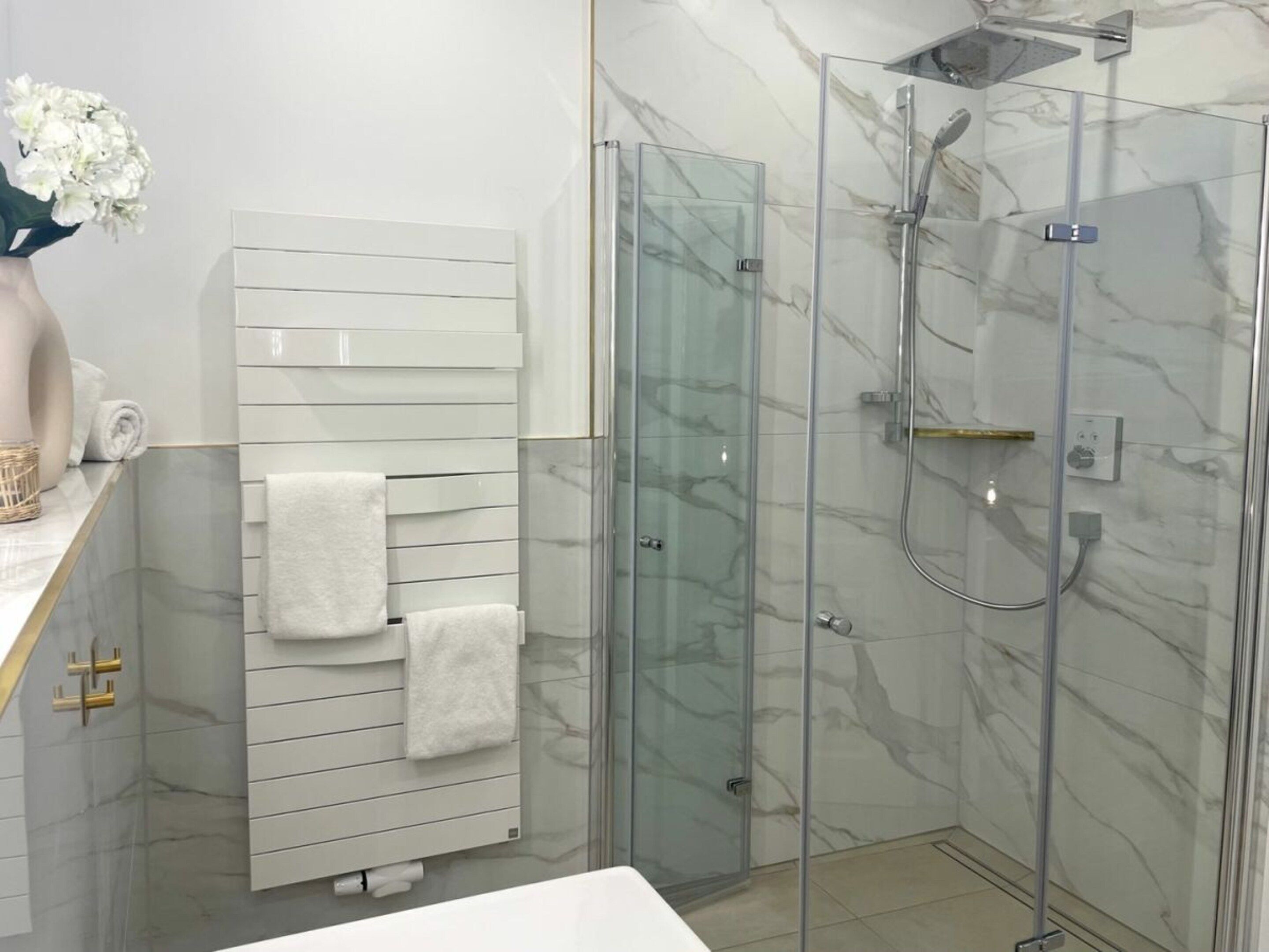 Un bagno moderno con doccia in vetro, portasciugamani bianco e parete rivestita in marmo.