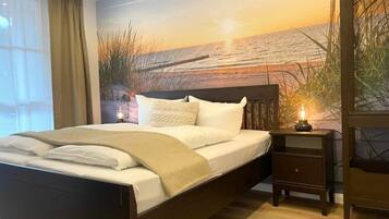 Un dormitorio con cama, una mesita de noche con lámpara y un mural en la pared que muestra un atardecer sobre el agua.