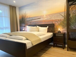 Un dormitorio con cama, una mesita de noche con lámpara y un mural en la pared que muestra un atardecer sobre el agua.