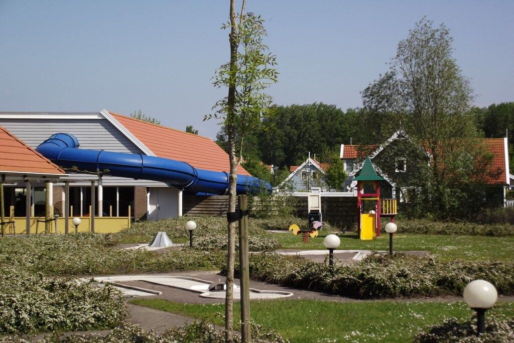 Ein Gebäude mit rotem Dach, einer blauen Struktur seitlich und einem Spielplatz mit einer gelben Rutsche.