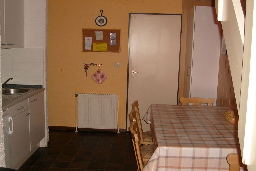 A compact kitchen with a sink, a white door, and a table with a checkered tablecloth.