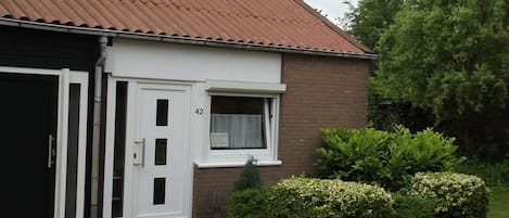 Una casa con puerta blanca, ventana con cortina y fachada de ladrillo.