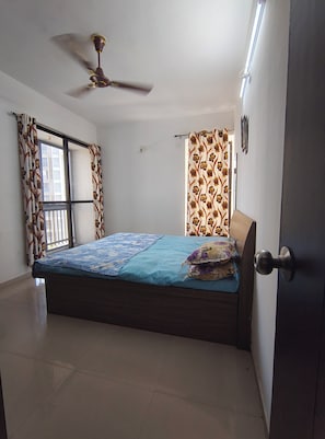 A bedroom with a bed, a ceiling fan, a window with curtains, and a door.