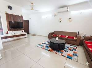 Ein modernes Wohnzimmer mit Flachbildfernseher, braunem Sofa, Couchtisch und einem gemusterten Teppich.