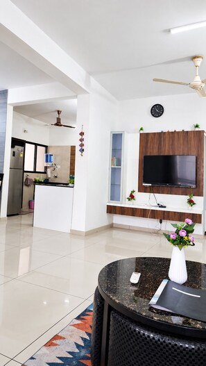 Un salon moderne avec un téléviseur à écran plat fixé à un mur en bois, un ventilateur de plafond et une table basse ronde sur laquelle est posé un vase de fleurs.