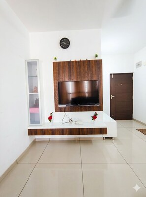 Un salon avec un téléviseur à écran plat fixé à un mur en bois, une console blanche en dessous et une porte sur la droite.