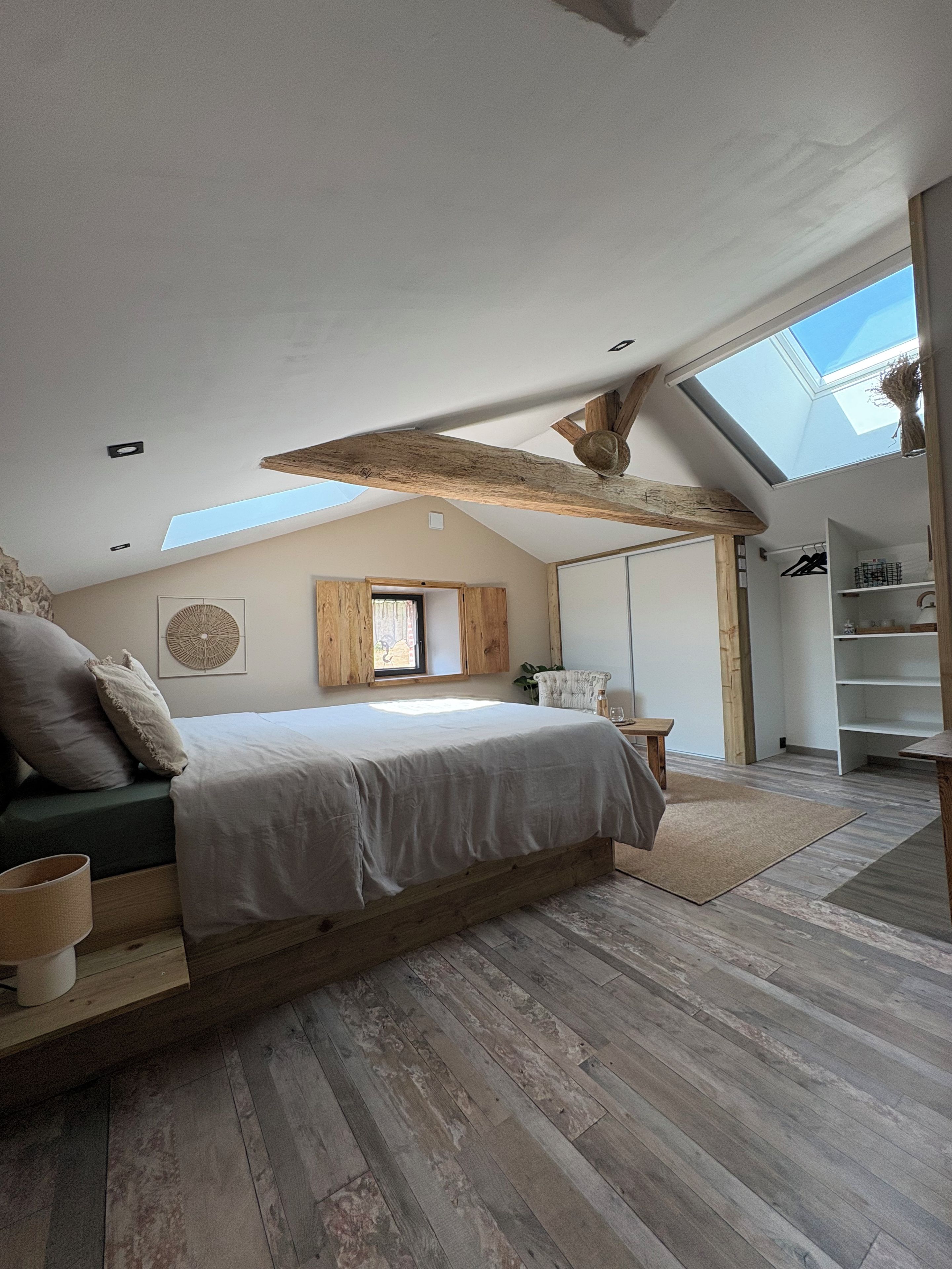 A bedroom with a sloped ceiling, a skylight, a bed with a wooden headboard, and a built-in wardrobe.