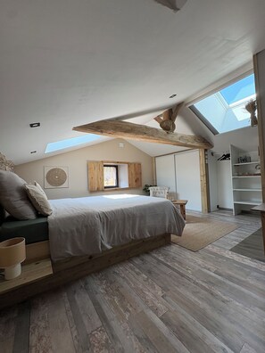 Un dormitorio con techo inclinado, tragaluz, cama con cabecera de madera y armario empotrado.