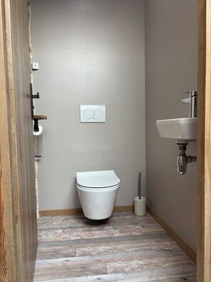 Un baño pequeño con inodoro, lavamanos empotrado y dispensador de papel higiénico.