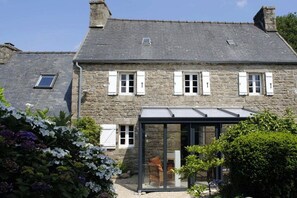 A stone building with a glass conservatory, a chimney, and a small window. - Breton stone house near the sea (Plounérin)