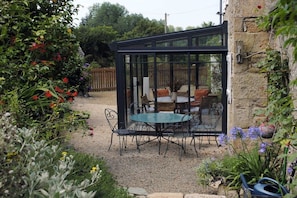 A conservatory with a glass roof, surrounded by a gravel path and various plants. - Breton stone house near the sea (Plounérin)