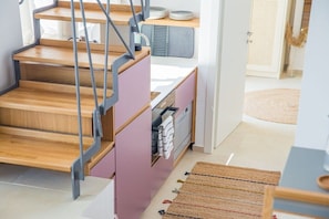 A staircase with a wooden finish and metal railings, leading to a kitchen area with pink cabinets and a countertop.