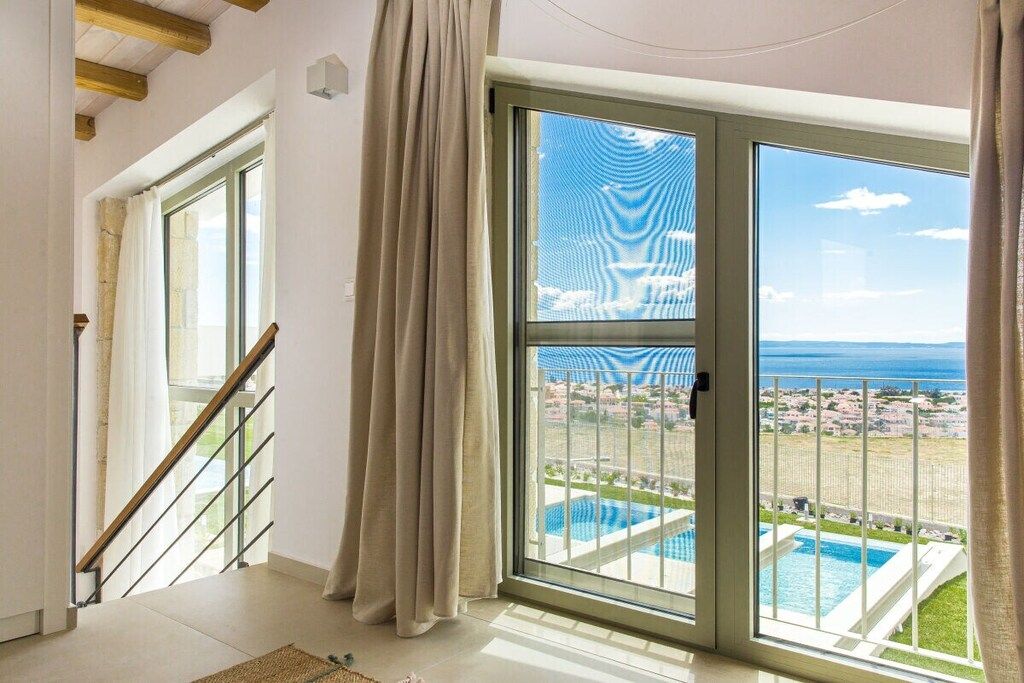 Una habitación con un amplio ventanal corredero que da a un balcón con piscina y vistas al mar.