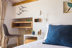 A bedroom with a bed, a chair, a nightstand, a wall-mounted shelf, and a wall clock.