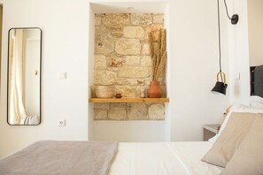 Un dormitori amb paret de pedra, un mirall, una estant amb objectes decoratius i un llit amb almoades.
