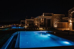 Zona de piscina de nit amb superfície d'aigua nítida, envoltada de murs de pedra i mobiliari d'exterior.