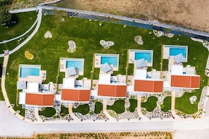 An aerial view of a hotel with multiple swimming pools, arranged in a row, surrounded by landscaped gardens and pathways.