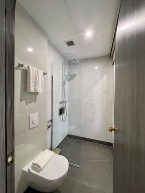 Et moderne badeværelse med bruseniche, toilet og håndklædestang.