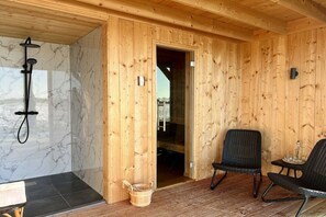 Ein Holzhütten-Interieur mit Dusche, zwei Stühlen und einem kleinen Tisch.