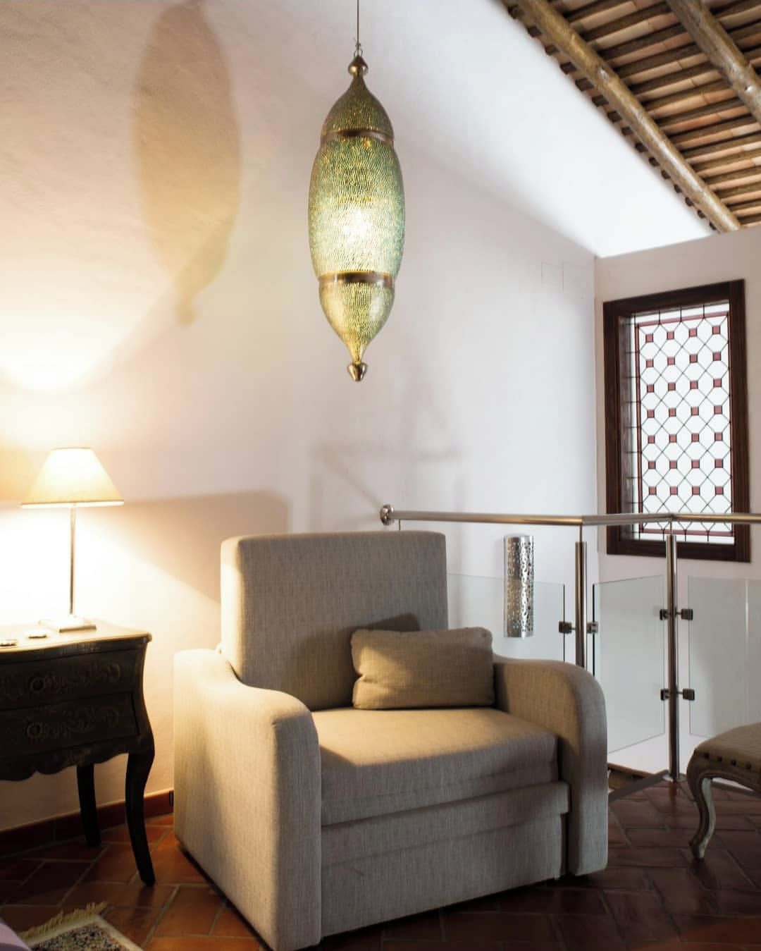 Una habitación con un sofá, una lámpara colgante, una ventana con diseño de cuadrícula y una lámpara en una mesita auxiliar.