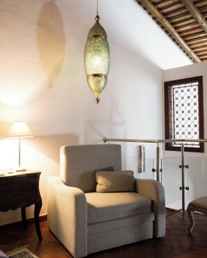 A room with a sofa, a hanging light fixture, a window with a grid pattern, and a lamp on a side table.