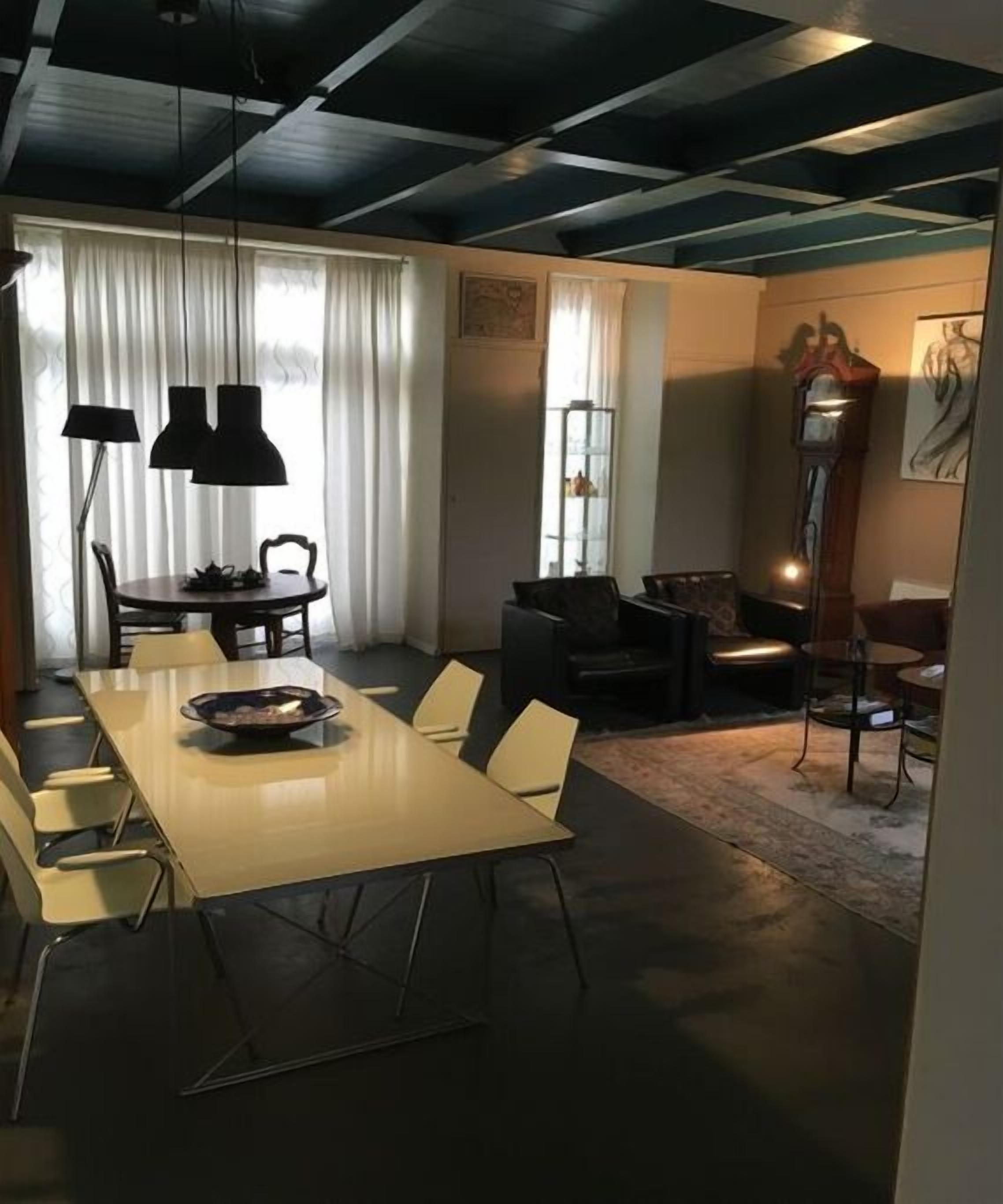 Een eetruimte met een lange tafel en stoelen, een kroonluchter en een klok aan de muur.